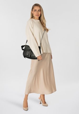 Beige gebreide trui met geribbelde zoom, gecombineerd met een vloeiende beige rok. Zwarte leren crossbodytas met een ronde gesp als detail.