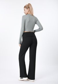 Haut court gris côtelé à manches longues, associé à un pantalon large côtelé noir et des baskets blanches avec des accents noirs.