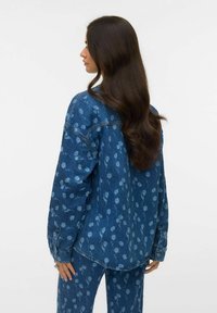 Farkkutakki, jossa on vaaleansininen kukkakuosi tummansinisellä taustalla. Takissa on rento istuvuus, pitkät hihat ja napilliset hihansuut.