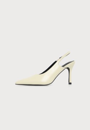 Kremowy, szpiczasty but na wysokim obcasie typu slingback z cienką szpilką i czarną podeszwą, widziany z boku.