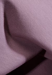 Mjukt, lätt tyg i en dämpad lavendelfärg, med en slät textur och subtil stretch, vilket framhäver ett fint stickat mönster.