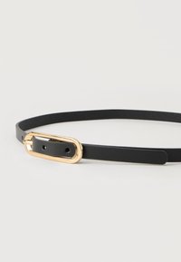 Ceinture fine en cuir noir avec une petite boucle rectangulaire dorée, posée à plat sur une surface blanche.