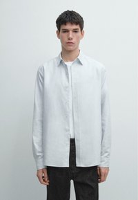 Camicia azzurra a bottoni realizzata in tessuto morbido, con colletto classico, maniche lunghe e taglio dritto, abbinata a jeans scuri.