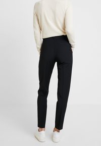 Schwarze, taillierte Hosen mit schmaler Passform, die eine glatte Textur, seitliche Taschen und einen cleanen Bund aufweisen, kombiniert mit weißen Sneakers.