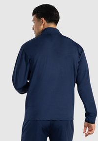 Polo de manga larga azul marino con un cuello alto, textura suave y un diseño ajustado. Presenta costuras tonal y puños elásticos.