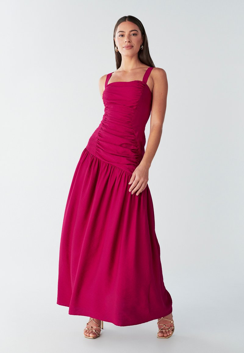 Vestido largo fucsia con un corpiño ajustado y fruncido, tirantes anchos y una falda fluida y recogida. Tela suave y silueta elegante.
