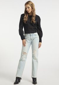 Sort tekstureret crop top med puffede ærmer, parret med lyseblå slidte jeans med revner. Sorte ankelstøvler fuldender looket.