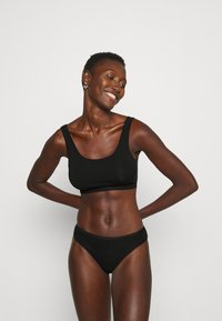 Zwarte naadloze beha en bijpassende slip, vervaardigd uit zachte materialen, met een ronde halslijn en een elastische tailleband voor comfort.