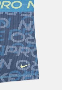 Top de sport Nike Pro en bleu foncé avec des rayures bleu clair et des motifs textuels. Il possède une taille élastique et un petit logo jaune.