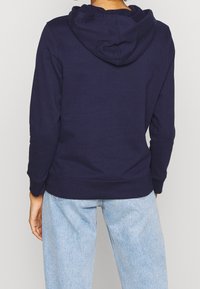 Felpa blu navy con cappuccio, dotata di un cordoncino regolabile, polsini e orlo a costine, con tasca a marsupio in un morbido tessuto texturizzato.