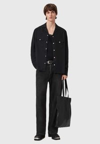 Sort skjorte med knapper og teksturerede detaljer, kombineret med sorte denimbukser og en sort taske med krokodillemønster.