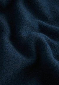 Tmavomodrá vlna, s jemnou textúrou a jemným leskom, zobrazuje mierne vlny a záhyby, čo zdôrazňuje jej hrúbku a teplo.