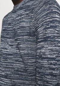 Sweter dzianinowy w ciemnym granacie z srebrnymi akcentami; posiada teksturowany, paskowany wzór oraz klasyczny okrągły dekolt.