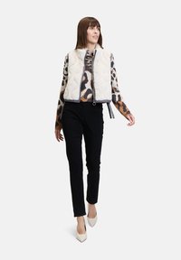 Gepolsterte Weste mit einem cremefarbenen, gesteppten Äußeren, ausgestattet mit einem Innenfutter aus Leopardenmusterwolle, Reißverschluss und schwarzen Hosen mit spitzen weißen Absätzen.