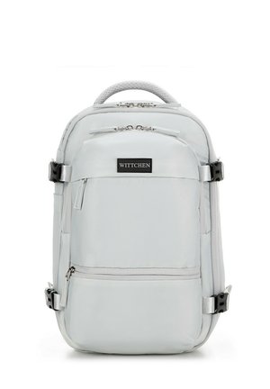 Mochila gris claro con múltiples compartimentos, cremalleras y correas ajustables. Presenta un asa texturizada en la parte superior y un parche con el logotipo de la marca.
