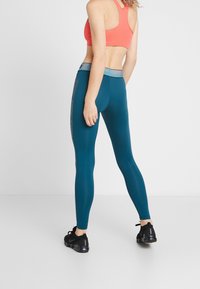 Leggings sportivi turchesi con una texture liscia, dotati di una fascia in un grigio chiaro a contrasto e inserti in mesh lungo i lati.