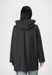 Giacca nera impermeabile con cappuccio, dal taglio rilassato, maniche lunghe e una texture liscia. Il design senza cuciture arriva fino a metà coscia.