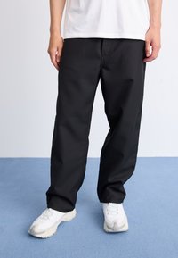 Black pants with a loose fit, made of smooth fabric. Features a straight leg design with front pockets and subtle stitching details.