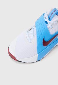 Nike basketball shoe in white with light blue accents. Features a textured upper and a maroon swoosh. Black rubber sole.