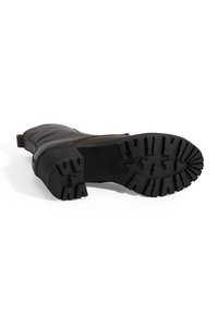 Bruine leren laars met een robuuste zwarte rubberen zool met diepe profielen. Het ontwerp omvat een zijpaneel en een lage, licht afgeronde hak.