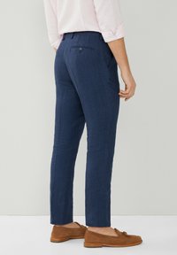 Pantaloni in lino blu navy con taglio dritto, dotati di una tasca posteriore singola e una trama sottile. Abbinati a scarpe slip-on marroni.
