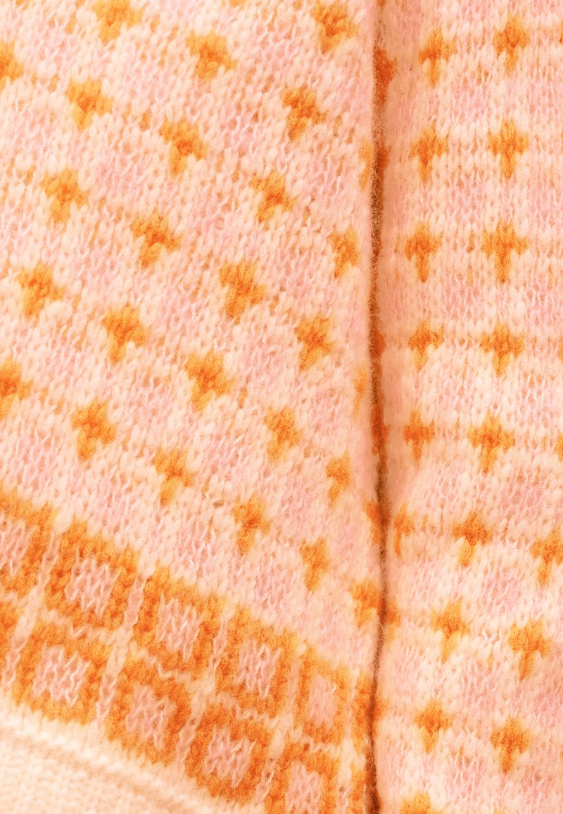 Le tissu tricoté présente une base rose clair avec des motifs d'étoiles et de losanges orange. Texture douce, apparence chaleureuse et coutures visibles partout.