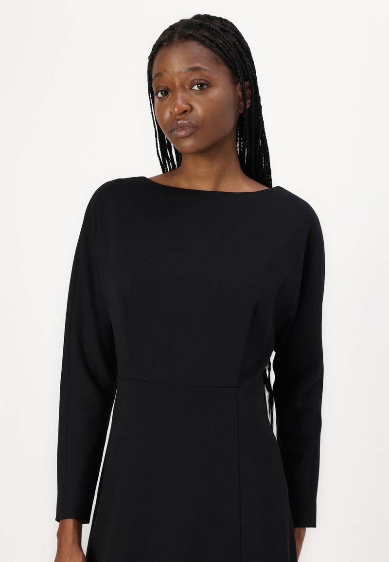 Schwarzes Langarmkleid mit einem Bootsausschnitt, figurbetontem Oberteil und glatter Textur. Entworfen für eine schlanke Silhouette, mit minimalistischem Detail.