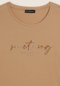 T-shirt beige realizzato in tessuto morbido, con testo glitterato "qualcosa di STUPENDO" in argento e oro, scollatura rotonda e maniche corte.