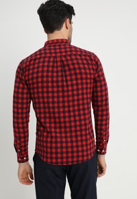 Camisa a cuadros roja y azul marino, de manga larga, con collar abotonado, dobladillo curvado, hecha de tela de algodón, cuenta con un yugo y detalles de botones.