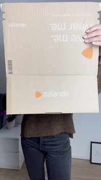Zalando kartonska kutija, svijetlosmeđa s narančastim logotipom. Ima preklopno zatvaranje i upute za rukovanje otisnute s jedne strane.