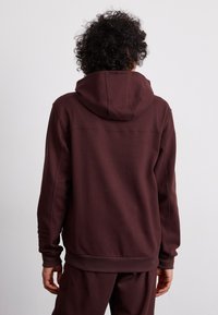 Felpa con cappuccio bordeaux in tessuto morbido, dal taglio rilassato, con tasca a marsupio e polsini e orlo ribattuti.