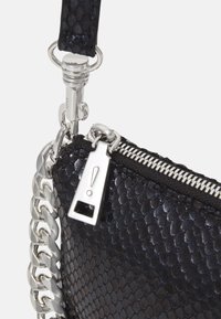 Sac en cuir noir texturé avec un motif de peau de reptile, une chaîne en métal argenté et une tirette de fermeture éclair argentée avec un accent en forme de point d'exclamation.