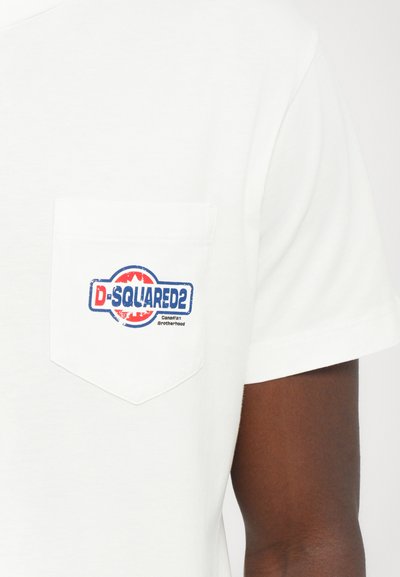 Camiseta de manga corta blanca hecha de algodón, con un bolsillo en el pecho que presenta un logo circular azul y rojo que dice "D-SQUARED2" y "Hermandad Canadiense."