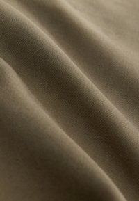 Nahaufnahme eines glatten, hellbraunen Stoffes mit weichen Falten und sichtbarer feiner Webstruktur bei sanfter Beleuchtung.