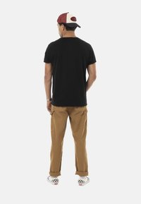 T-shirt noir à col rond, pantalon cargo beige avec poches et chaussures à enfiler à carreaux. La casquette présente un schéma de couleurs rouge et crème.