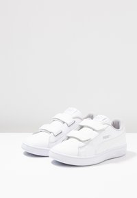 Sneakers bianchi con una superficie in pelle liscia, doppi cinturini in Velcro, collo imbottito e dettagli testurizzati sui lati.