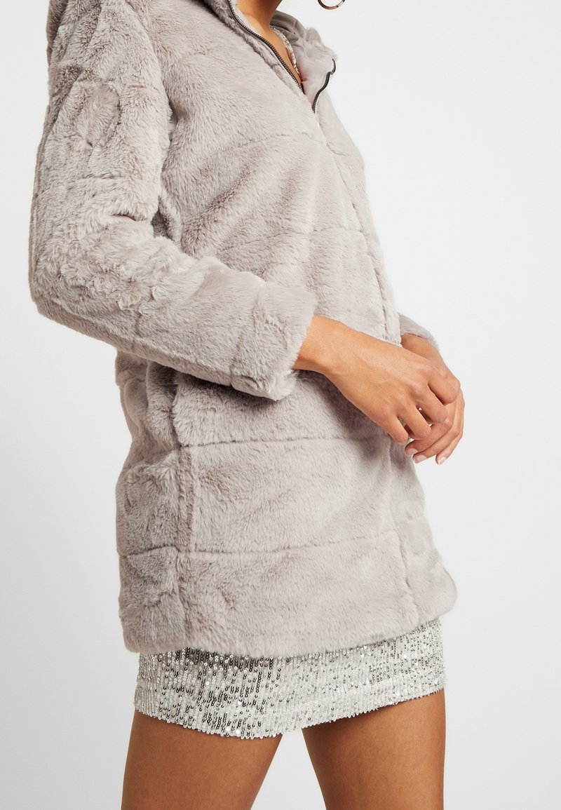 Lys grå faux fur jakke med lynlås foran, præget med en tekstureret overflade og lange ærmer, parret med en glitrende sølv mini nederdel.