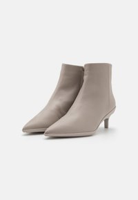 Botas de tobillo de punta afilada en suave cuero beige con una textura lisa, que cuentan con un tacón bajo y un cierre lateral de cremallera.