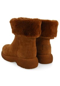 Botines de ante marrón con un puño de piel sintética, que cuentan con una suela de goma texturizada y una discreta etiqueta de la marca en el lateral.