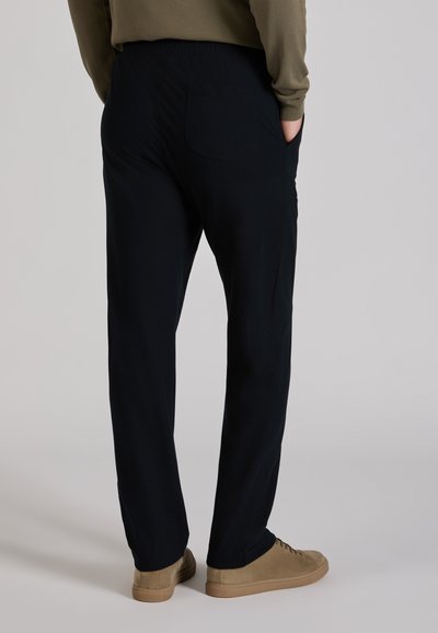 Czarne spodnie z elastycznym pasem i tylną kieszenią, wykonane z gładkiego materiału. Połączone z jasnobrązowymi butami. Neutralne tło.