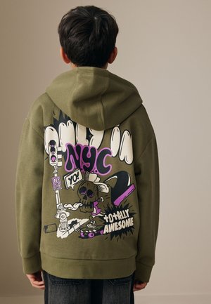 Enfant vu de dos portant un sweat à capuche vert olive avec un graffiti coloré style NYC, personnage en skateboard, et le texte « totally awesome » au dos.