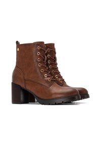 Botas de cuero marrón hasta el tobillo con un tacón grueso, que presentan ojales dorados, cordones y una suela de goma negra texturizada.