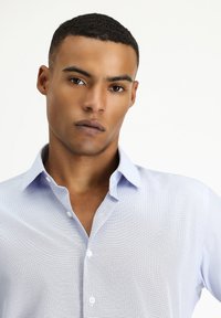 Camicia button-up azzurra chiara realizzata in un tessuto texturizzato, con colletto a punta e bottoni bianchi, caratterizzata da un delicato motivo a griglia.