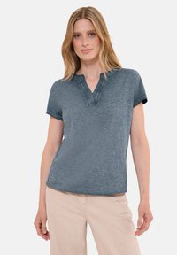 T-shirt a maniche corte e scollo a V in tessuto blu melange. Caratterizzato da una vestibilità comoda e una consistenza morbida con orli arrotolati. Indossato con pantaloni chiari.