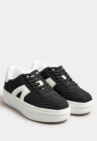 Svarta och vita sneakers med en slät, matt finish. Har en tjock vit sula och enskilt skärdesigner på sidorna.