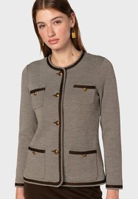 Skräddarsydd kavaj i hundtandsmönster, krämiga och bruna färger, rund halsringning, guldfärgad knappar, två bröstfickor och kontrasterande kant.