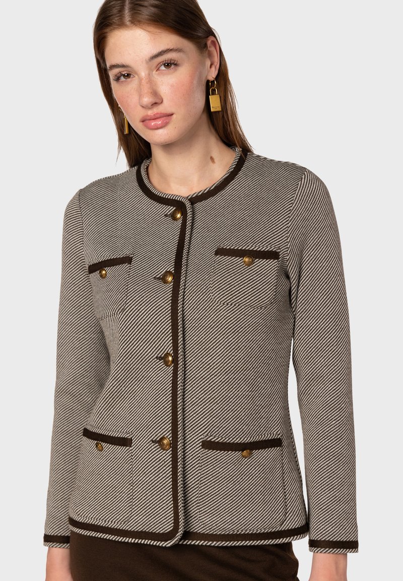 Skräddarsydd kavaj i hundtandsmönster, krämiga och bruna färger, rund halsringning, guldfärgad knappar, två bröstfickor och kontrasterande kant.