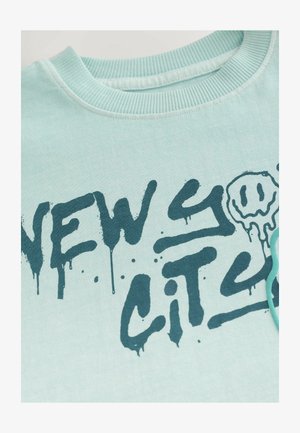 Jasnoniebieska bawełniana koszulka z ciemnoniebieskim tekstem w stylu graffiti "NOWY JORK" z kroplami i okrągłymi akcentami graficznymi w kształcie uśmiechniętej buźki.