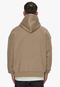 Hoodie in einem hellbraunen Farbton, aus weichem Material mit lockerer Passform, ausgestattet mit einer großen Kapuze und Rippbündchen.