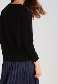 Czarny dzianinowy sweter z długimi rękawami i okrągłym dekoltem, w połączeniu z plisowaną granatową spódnicą. Miękka tekstura i casualowy design.